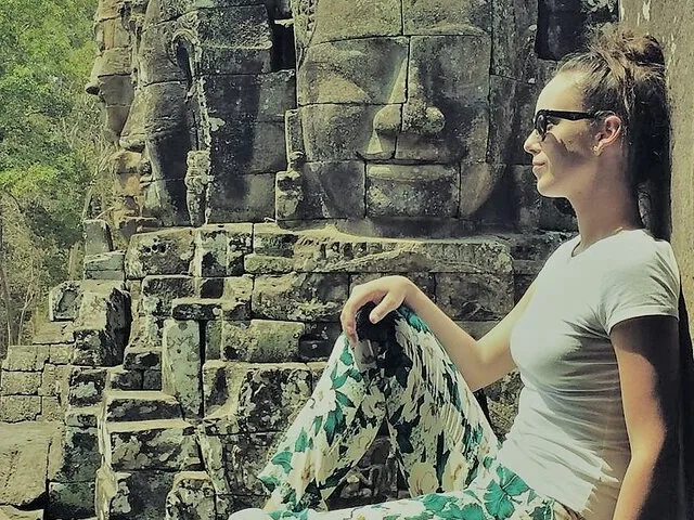 Donna seduta vicino ad antichi volti in pietra scolpiti nelle rovine del tempio