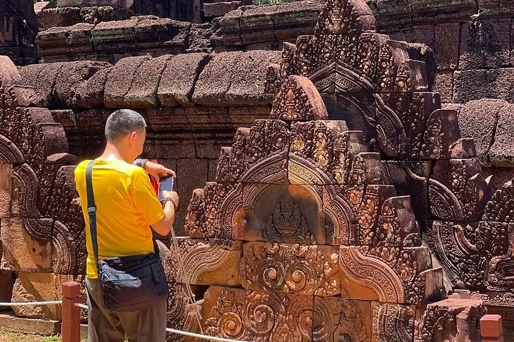 Turista che scatta una foto agli intricati intagli in arenaria a Banteay Srei